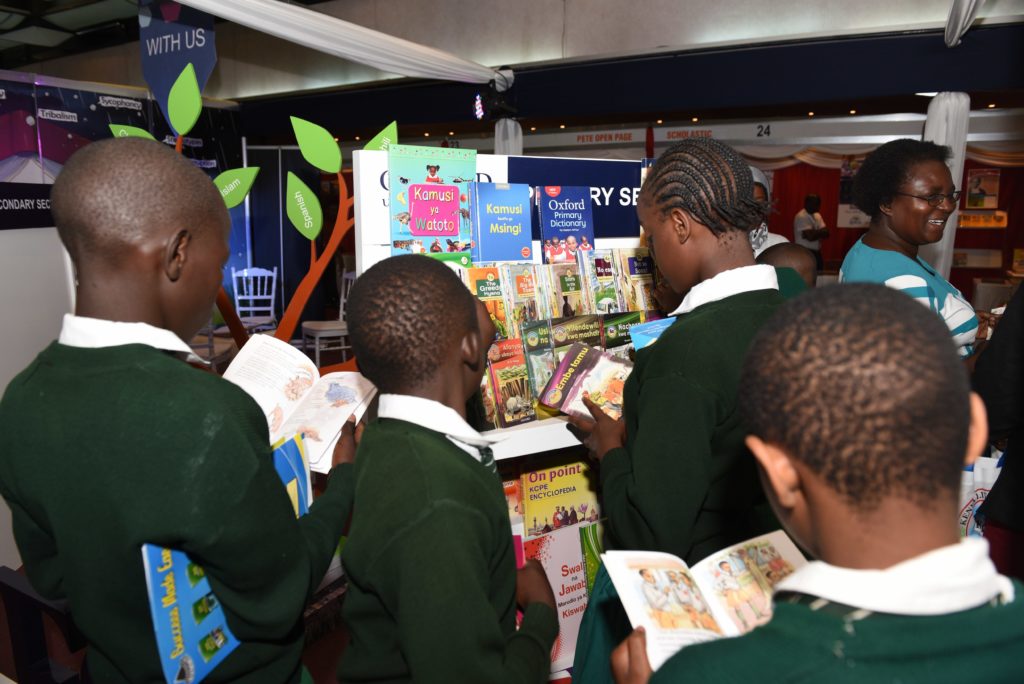 Vihreään koulupukuun puketuneita koululaisia selaamassa kirjoja hyllyn edessä.