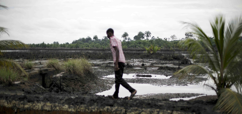 Mies kävelee jokisuistossa, jonka öljyvuodot ovat värjänneet mustaksi.