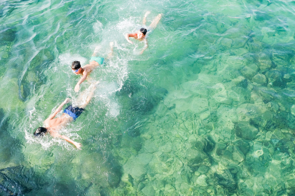 Kolme poikaa ui vihreässä meressä.