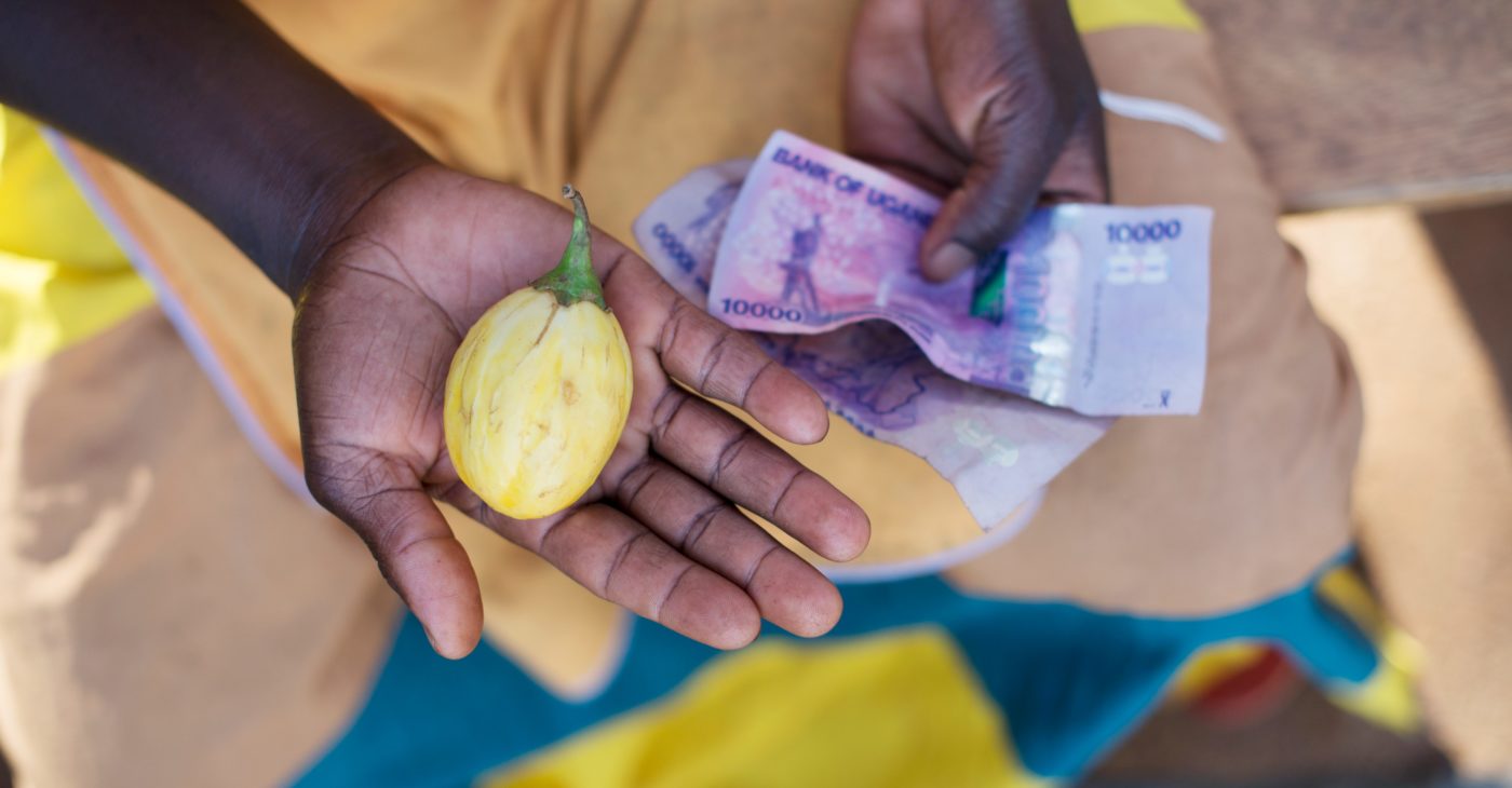 Naisen kädessä Ugandan seteleitä ja keltainen hedelmä.