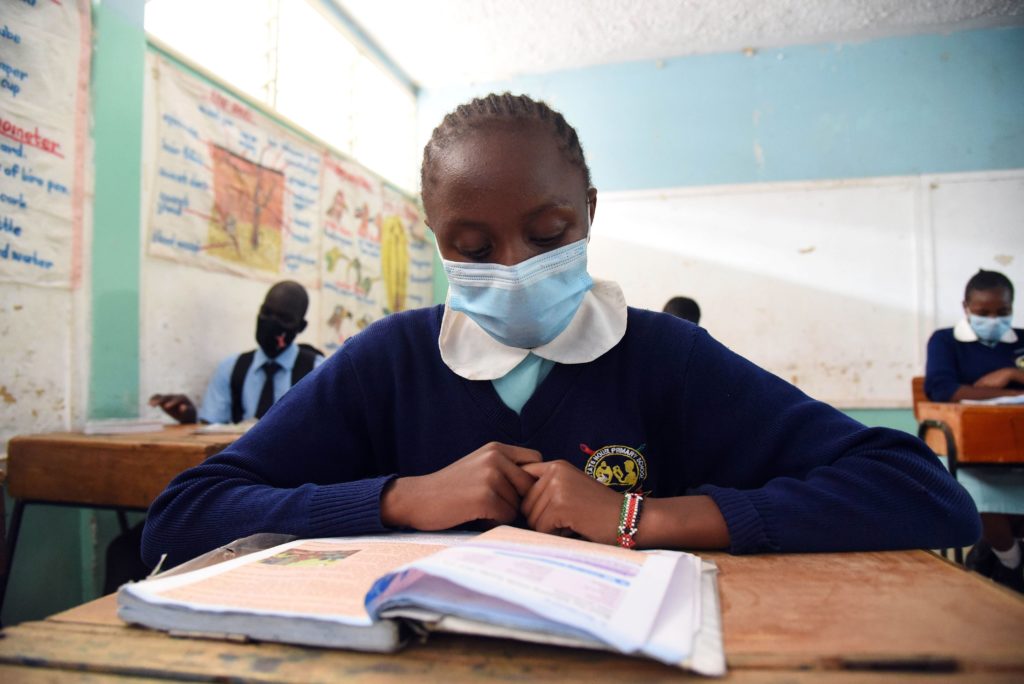 Maskiin pukeutunut tyttö lukee kirjaa luokkahuoneessa Keniassa, Nairobissa.