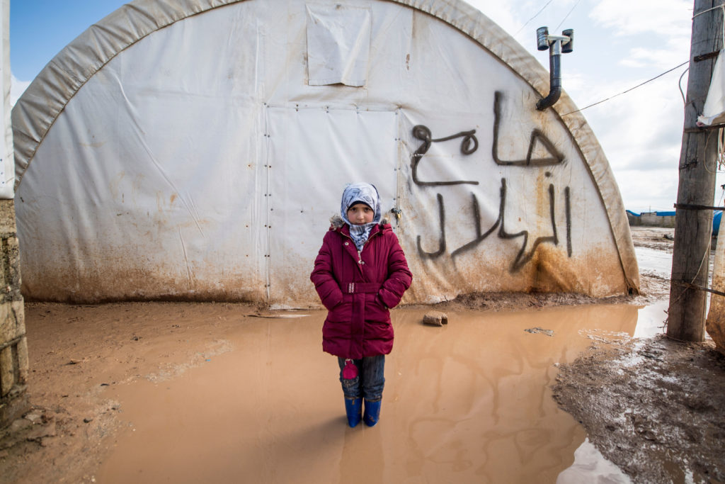 Tyttö seisoo vesilammikossa pakolaisteltan edessä Syyriassa.