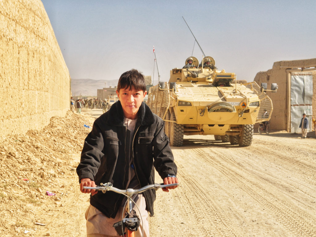 Poika pyöräilee taustallaan panssarivaunu.