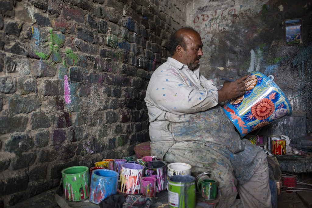 Mies maalaa ämpäriä värikkäin kuvioin vieressään maalipurkkeja.