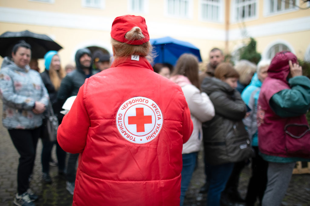 Naisella punainen toppatakki, jonka selässä Punaisen Ristin tunnus ukrainaksi.