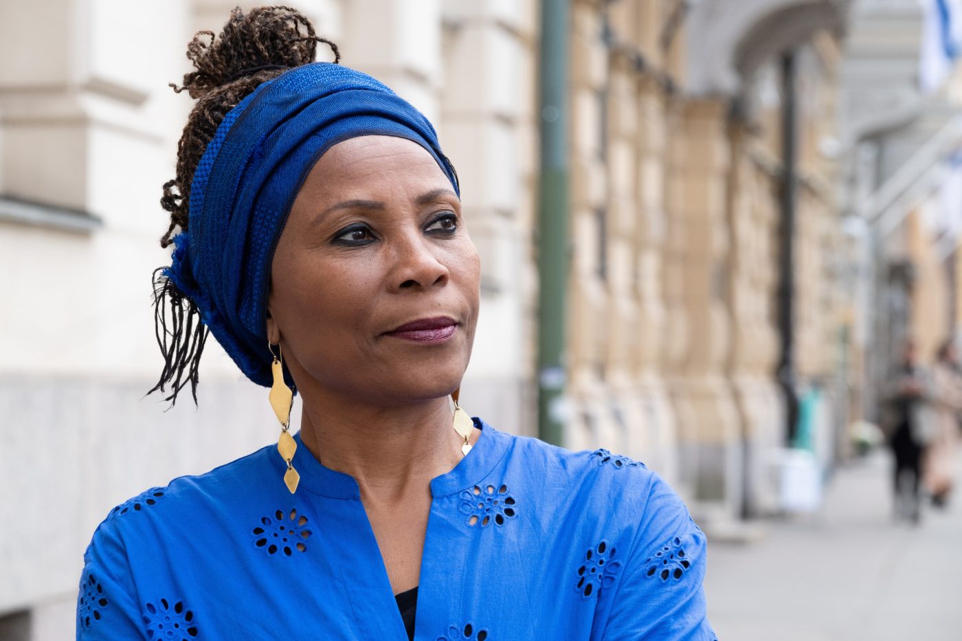 Keski-ikäinen afrikkalaisen näköinen nainen katsoo eteenpäin, sininen leveä huivi päässä.