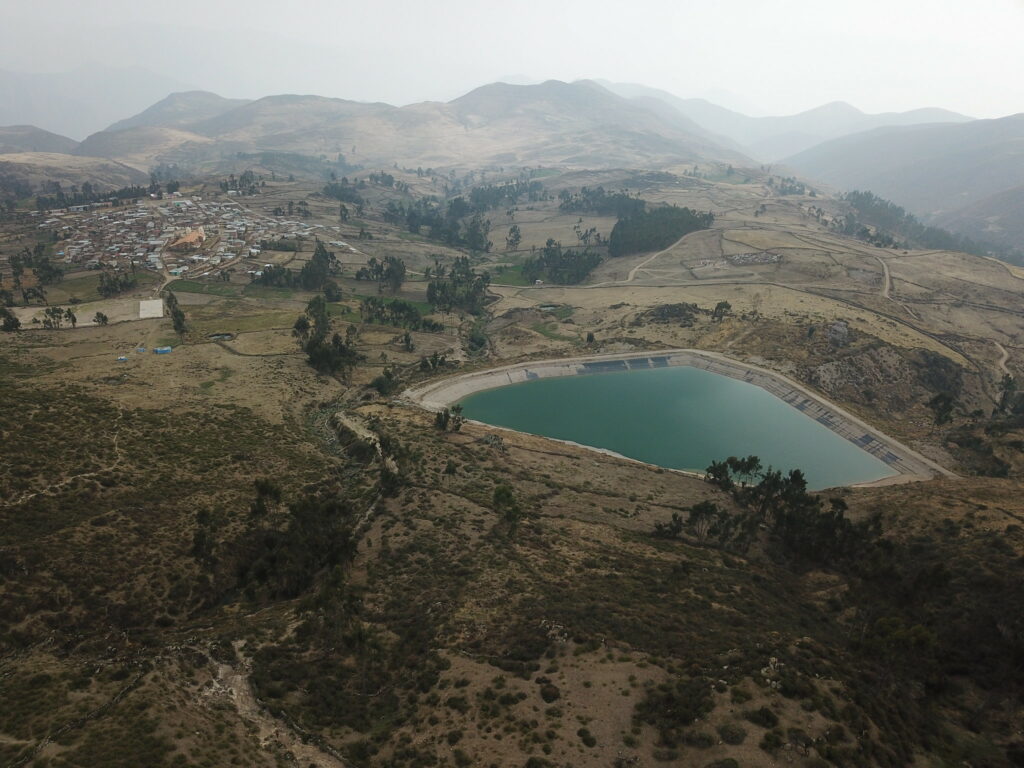 Andien vuoristomaisemaa. Edustalla isohko lähde, johon on kerääntynyt vuorenrinteeltä alas ohjautunutta vettä. Taustalla asuinkylä.