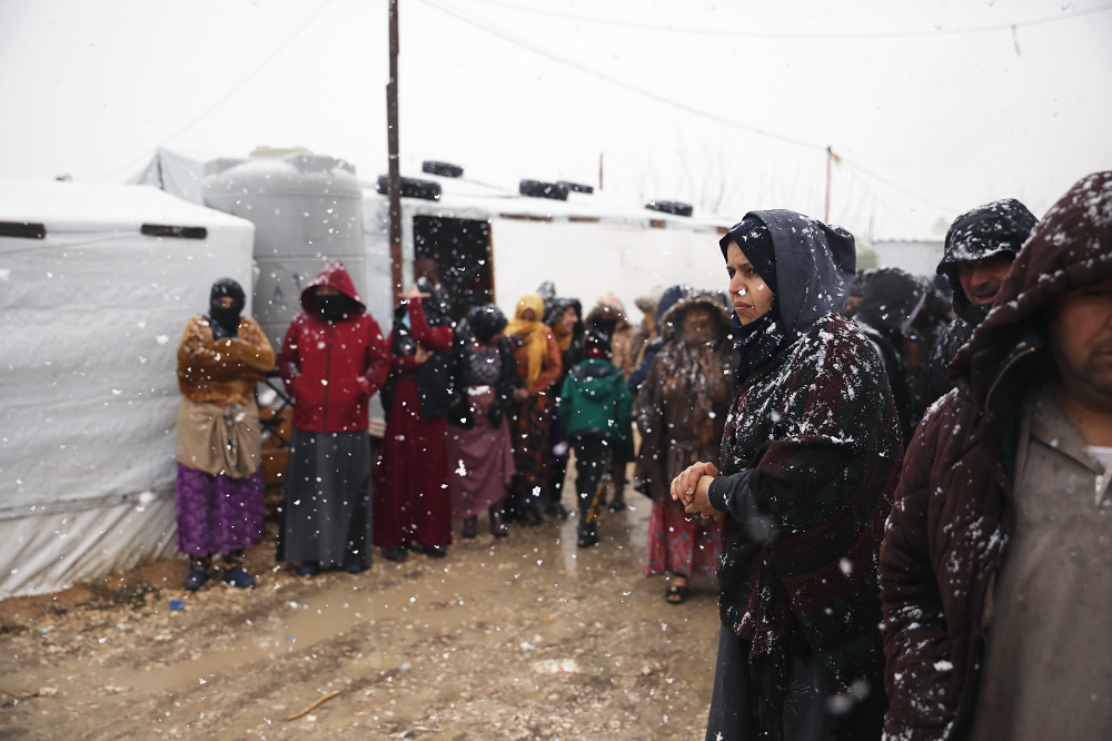 Värjötteleviä aikuisia lumisateessa, pakolaisleirillä.