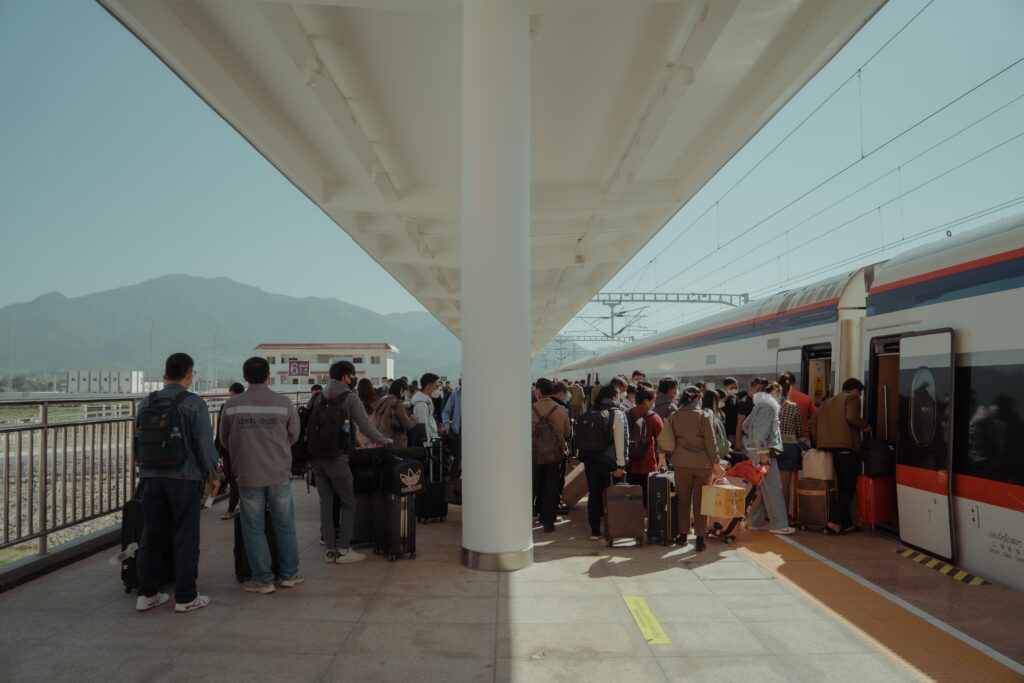 Asemalaiturilla ihmisiä menossa junaan, taustalla vuori.