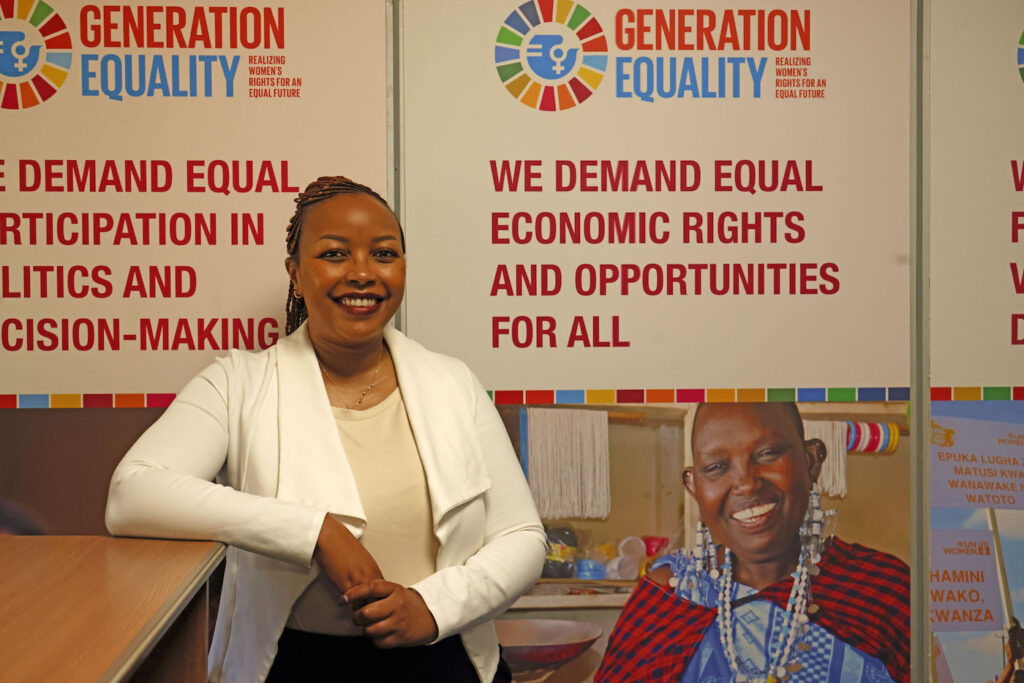 Ellen Muchunu nojaa pöytään taustallaan YK-järjestön julisteita.