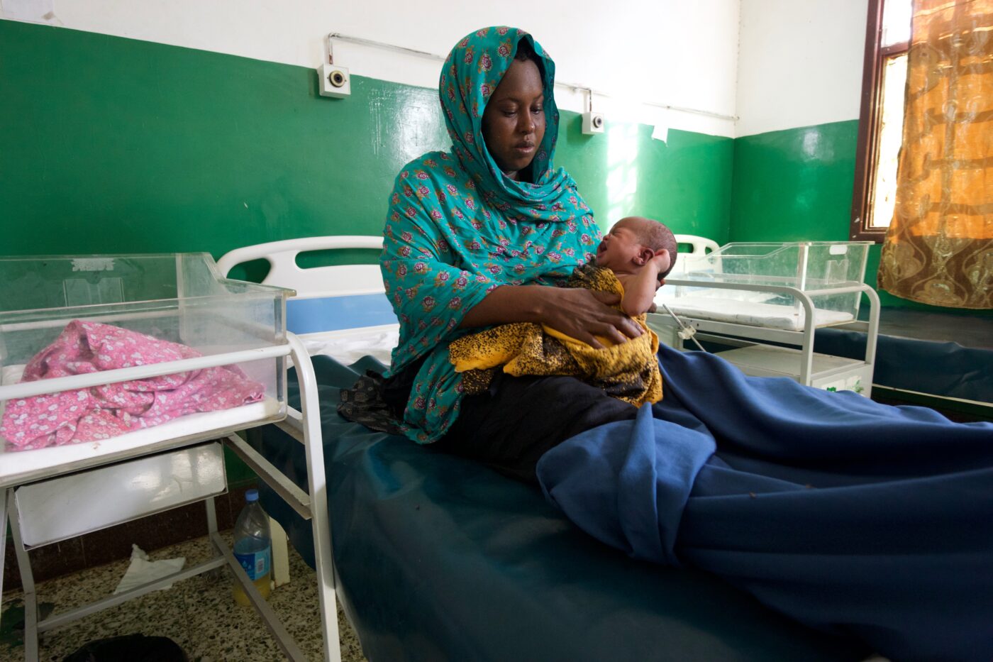 Huivipäinen nainen istuu sairaalasängyllä pidellen vauvaa.