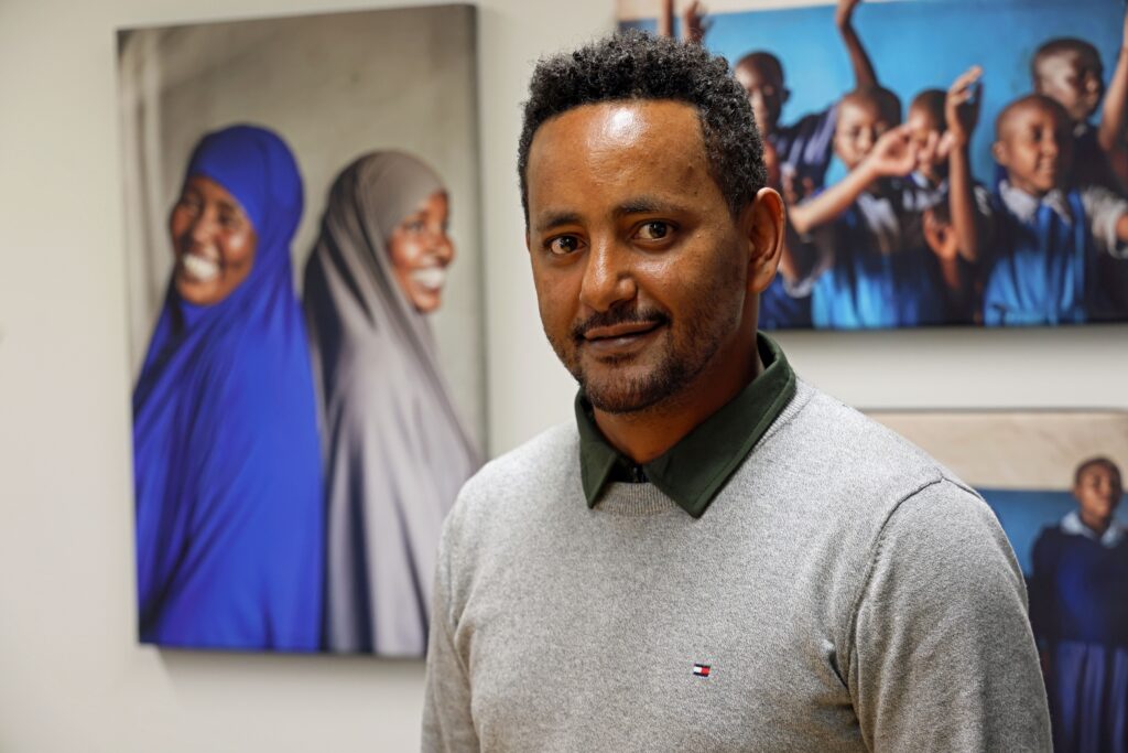 Mies katsot kameraan, taustalla kuvia huivipäisistä ehkä somalinaisista.