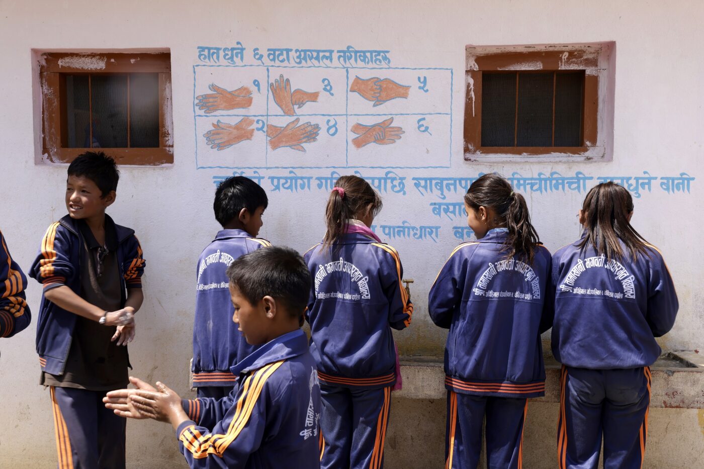 Joukko lapsia pesee käsiään, taustalla rakennuksen seinään on piirretty ohjeet käsienpesusta.