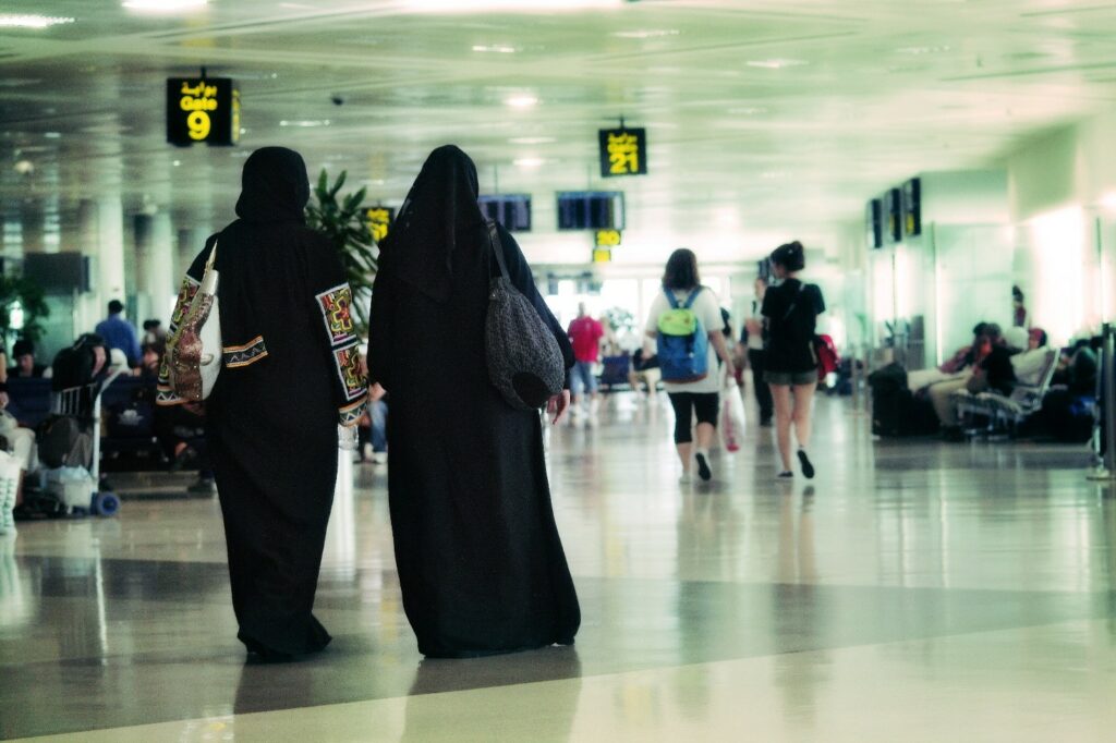 Kaksi peittäviin mustiin vaatteisiin pukeutunutta naista lentokentältä näyttävässä hallissa.