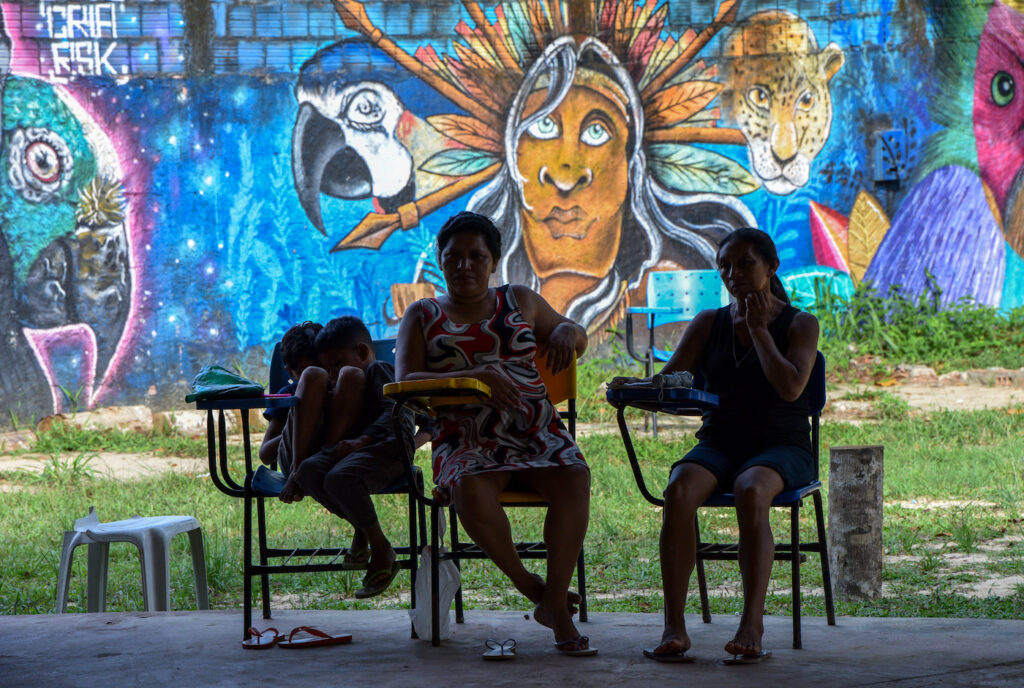 Värikkään graffitin edessä kolme ihmistä istuu tuoleilla varjossa.