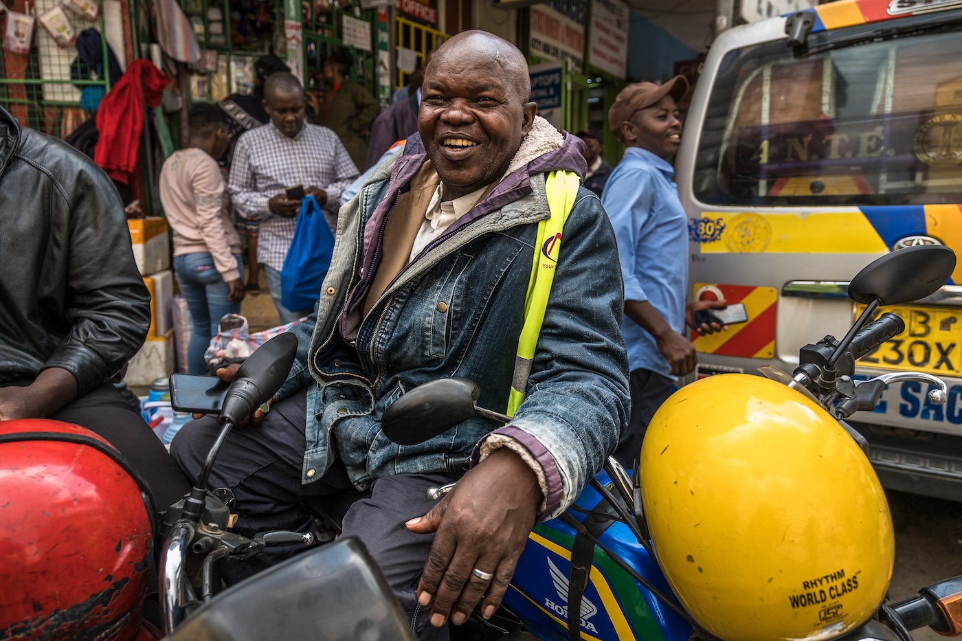 Mies istuu moottoripyörän päällä ja hymyilee vieressään keltainen moottoripyöräkypärä.