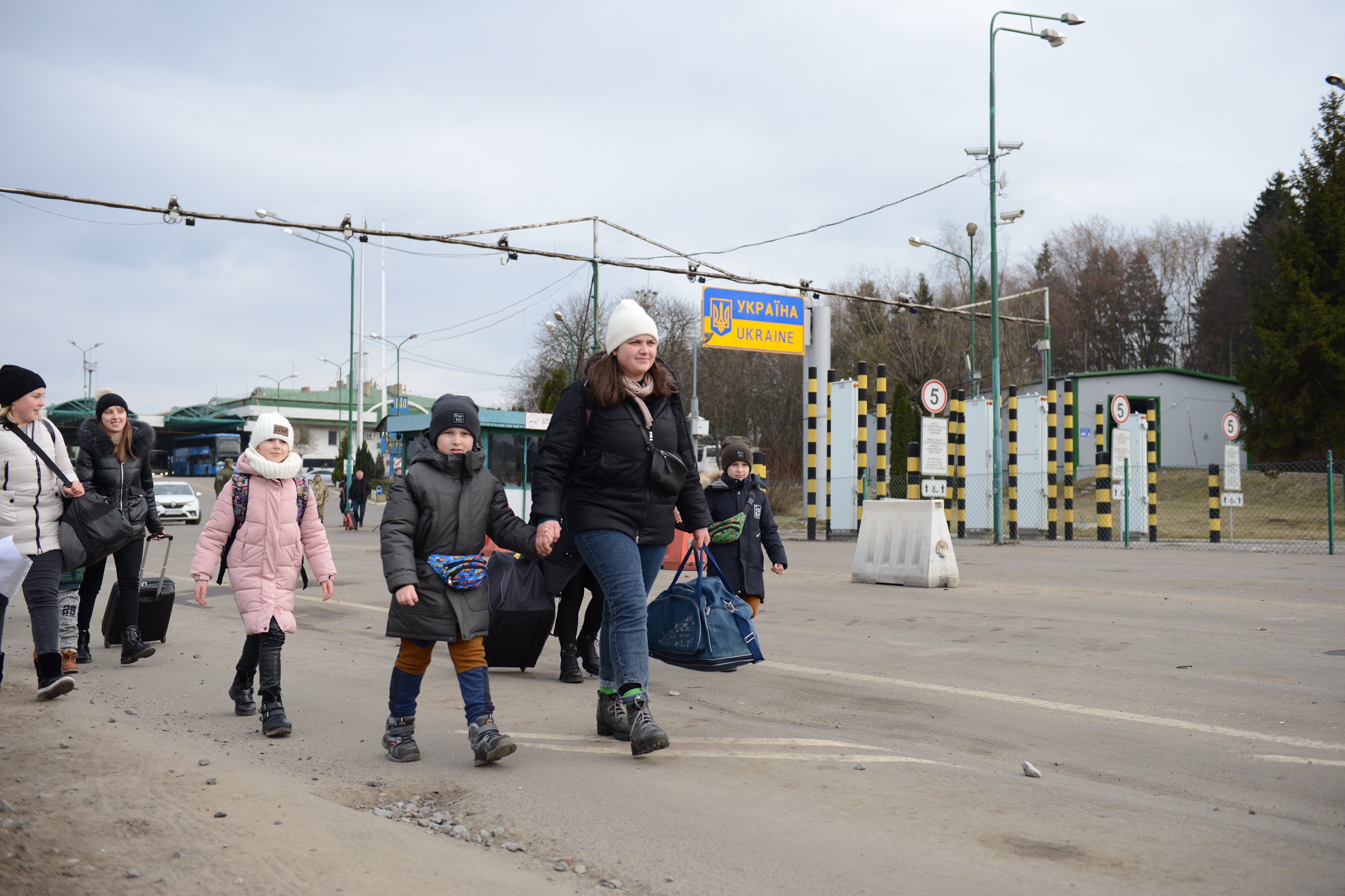 Nainen ja lapsia talvivaatteissa ylittämässä raja-asemaa.