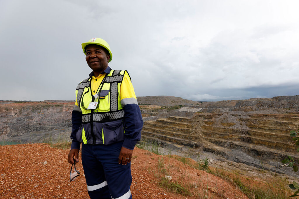 Keltaiseen kypärään ja työasuun pukeutunut mies seisoo pengerretyn kaivoksen edessä.