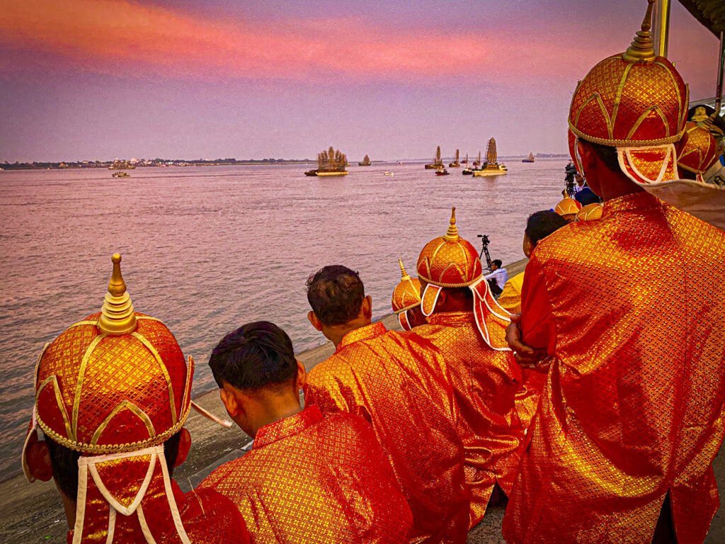 Kultaoransseihin pukuihin juhla-asuihin pukeutuneet miehet seuraavat veneitä joella.
